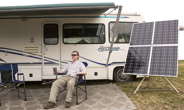 Man sitting outside of RV beside a panel of solar batteries